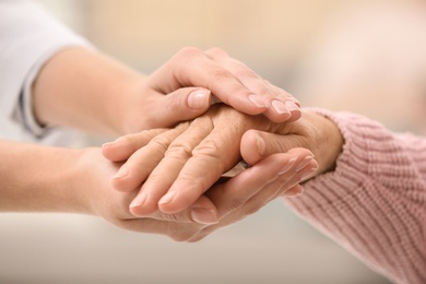 Photo of Nurse holding hands of elderly woman against blurred background, closeup. Assisting senior generation