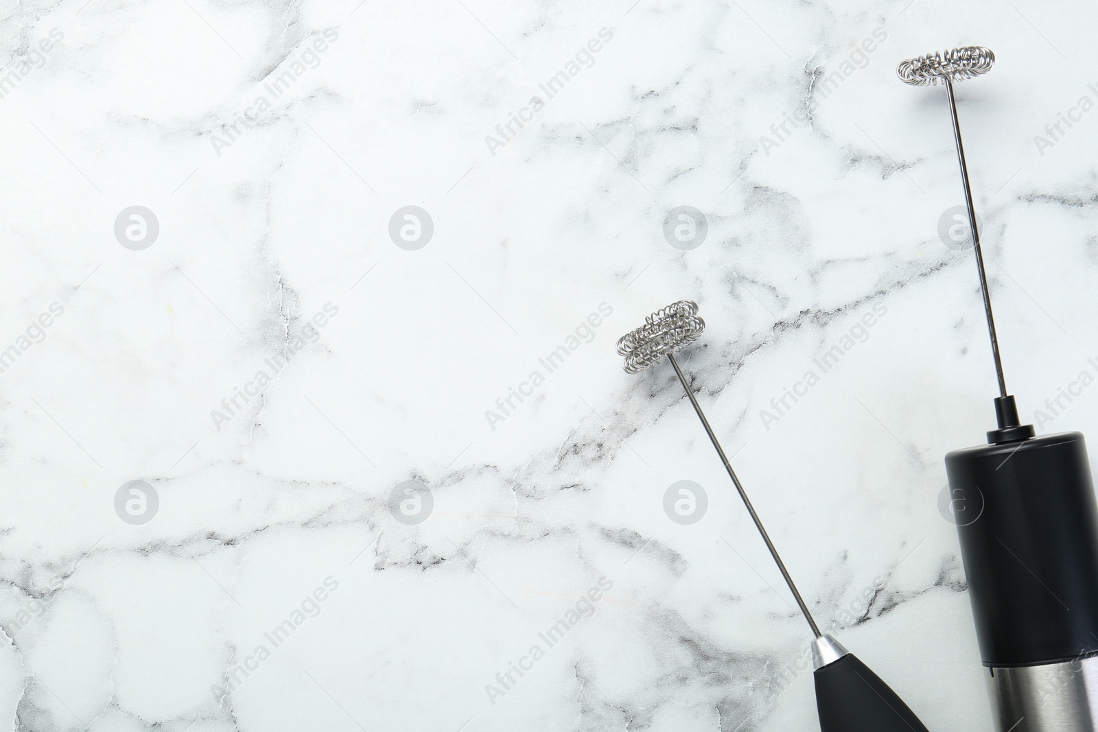 Photo of Black milk frother wands on white marble table, top view