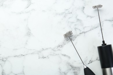 Black milk frother wands on white marble table, top view