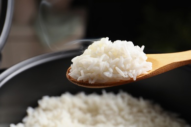 Spoon with tasty hot rice over cooker, closeup