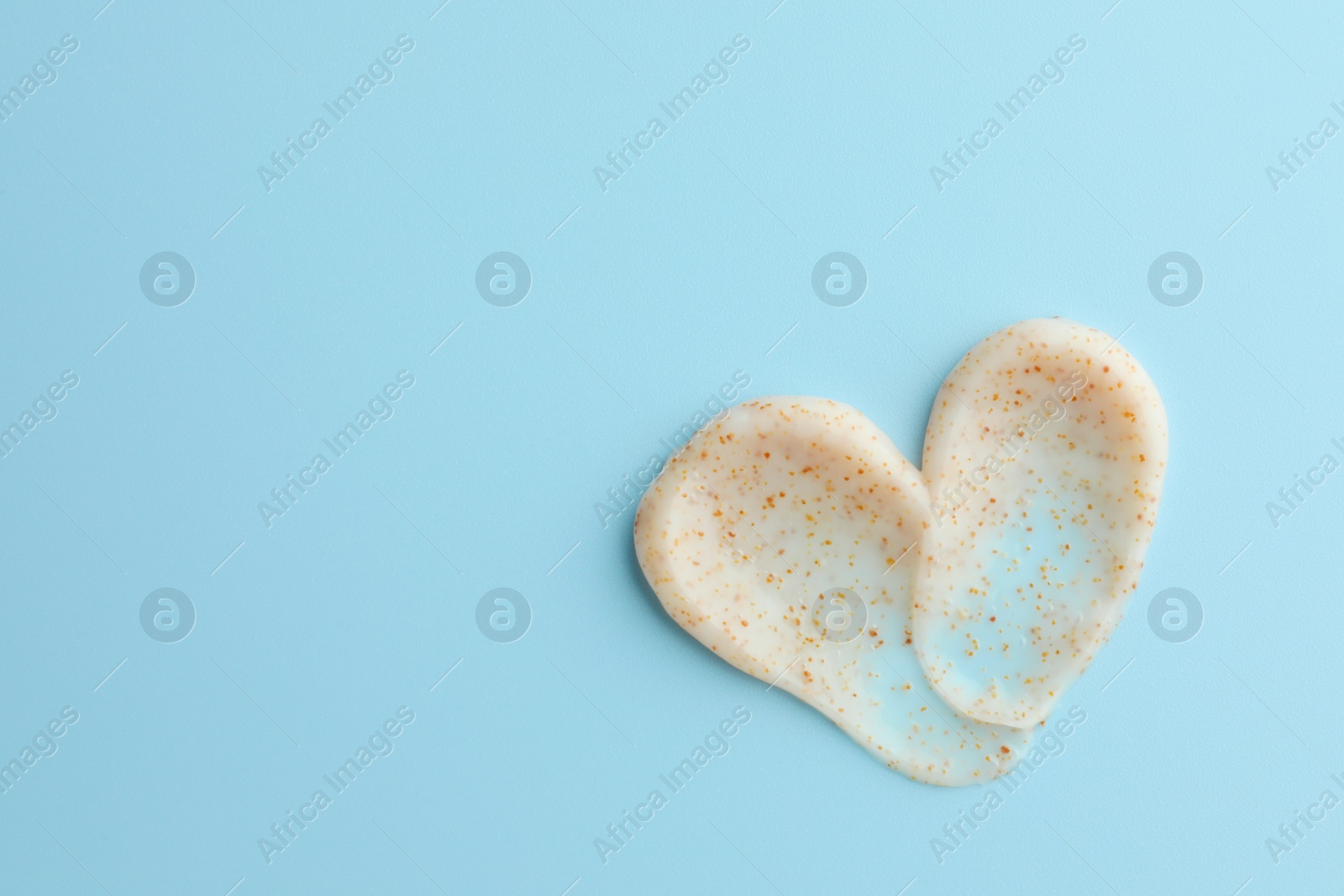Photo of Samples of face scrub in shape of heart on light blue background, top view. Space for text