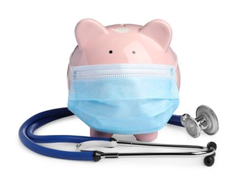 Photo of Piggy bank in protective mask and stethoscope on white background. Medical insurance