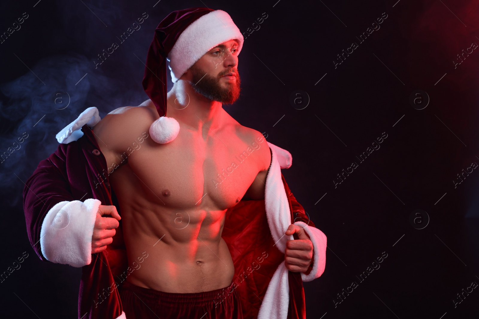 Photo of Attractive young man with muscular body in Santa costume on black background, space for text
