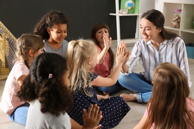 Photo of Cute little children with nursery teacher in kindergarten. Indoor activity