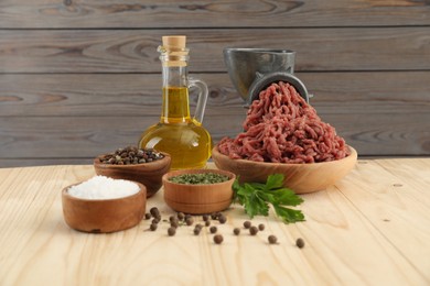 Photo of Mincing beef with manual meat grinder. Parsley, oil and spices on wooden table