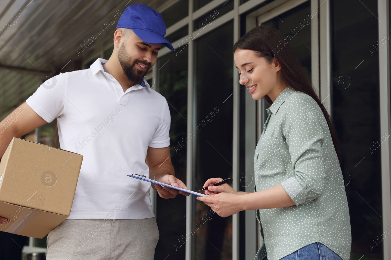 Photo of Woman signing for delivered parcel near entrance outdoors