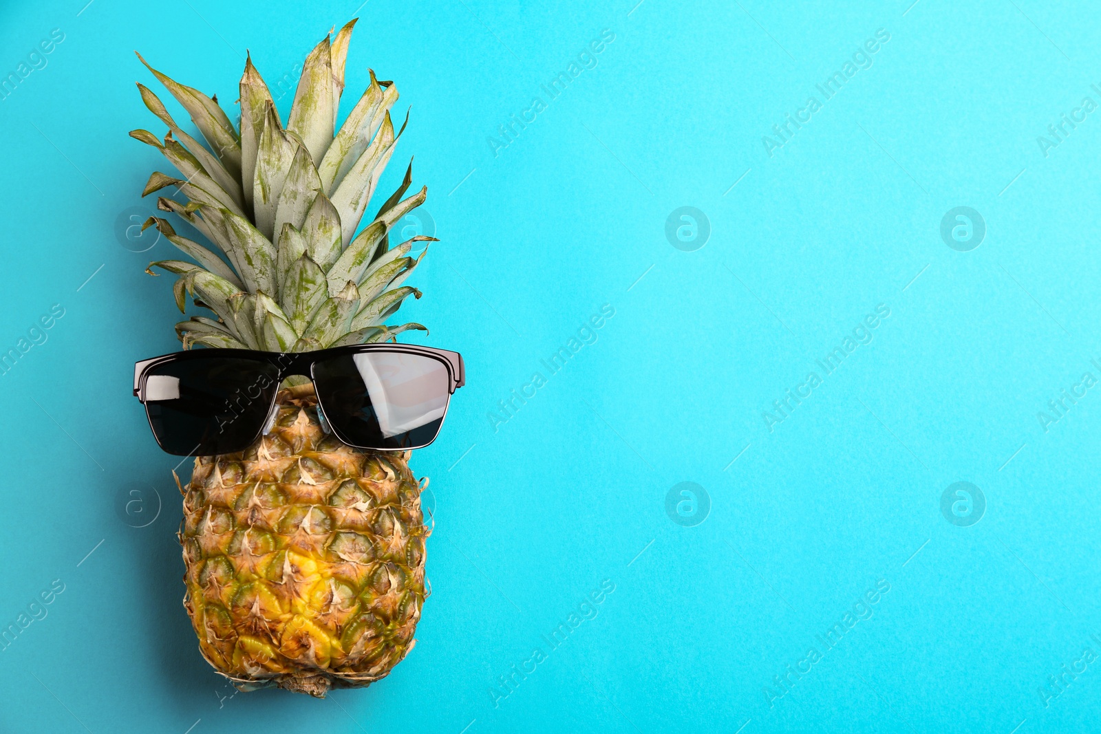 Photo of Pineapple with sunglasses on blue background, top view. Space for text