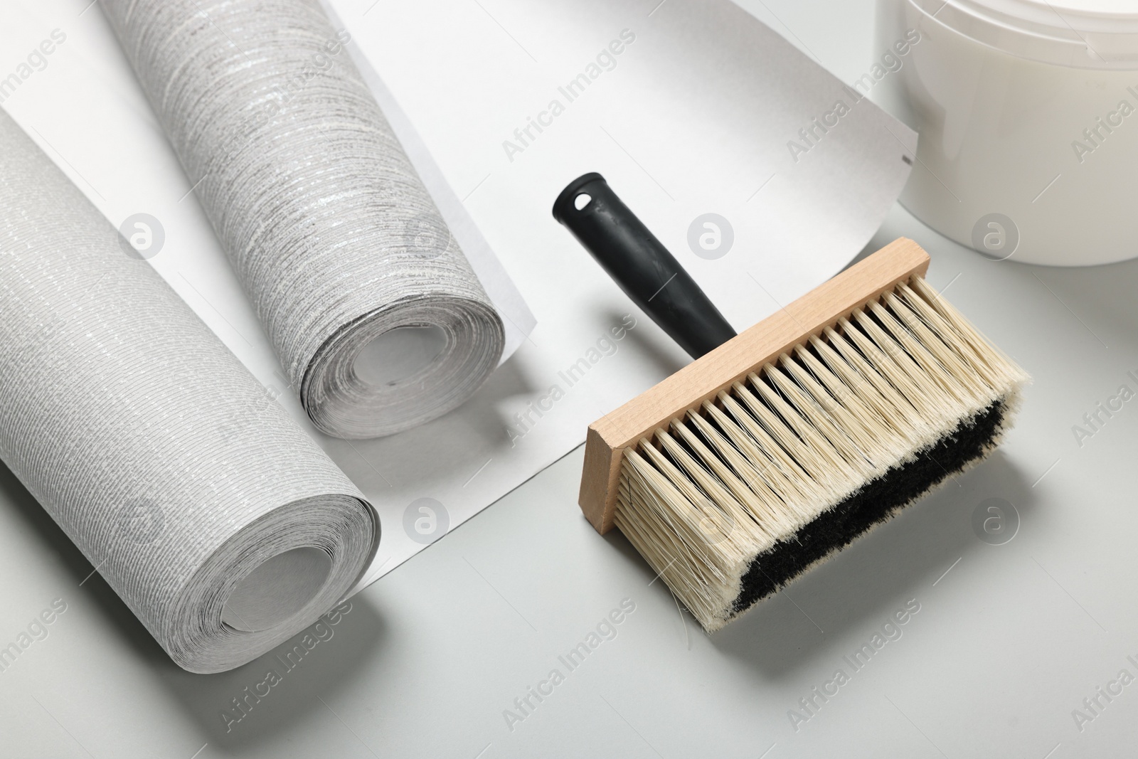 Photo of Different wallpaper rolls and brush on light grey background