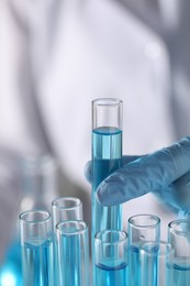 Photo of Scientist taking test tube with light blue liquid in laboratory, closeup