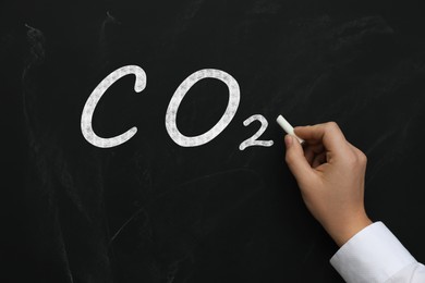 Image of Reduce carbon emissions. Woman writing chemical formula CO2 on blackboard, closeup