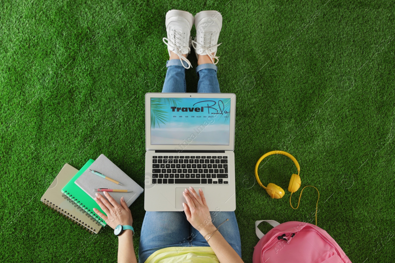 Photo of Woman holding laptop with open travel blogger site on artificial grass, top view