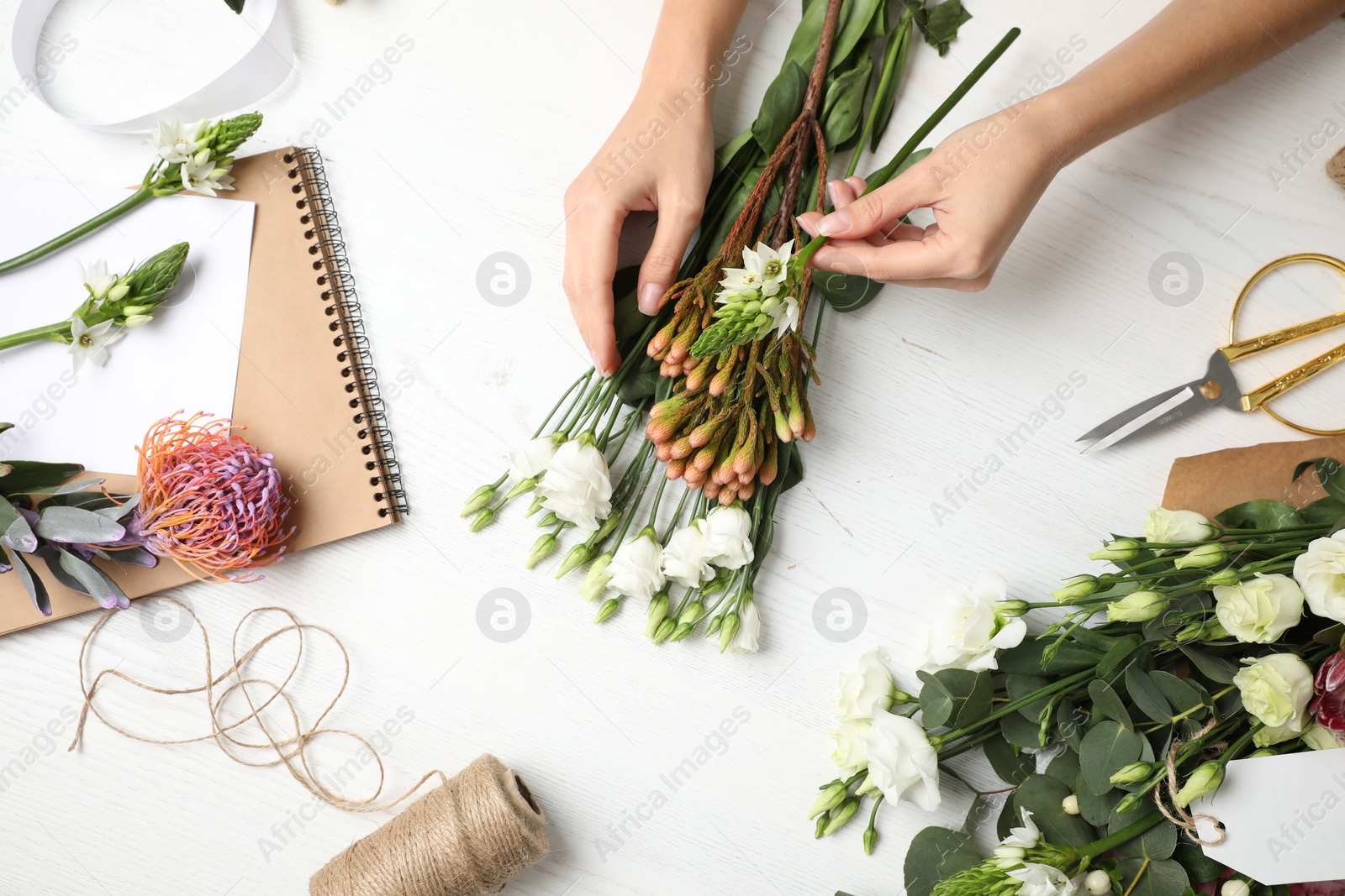 Photo of Florist making beautiful bouquet at white wooden table, top view