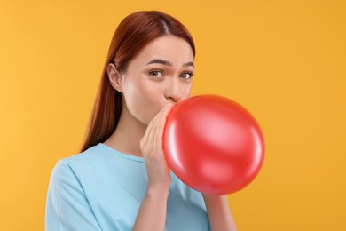 Photo of Woman inflating red balloon on orange background