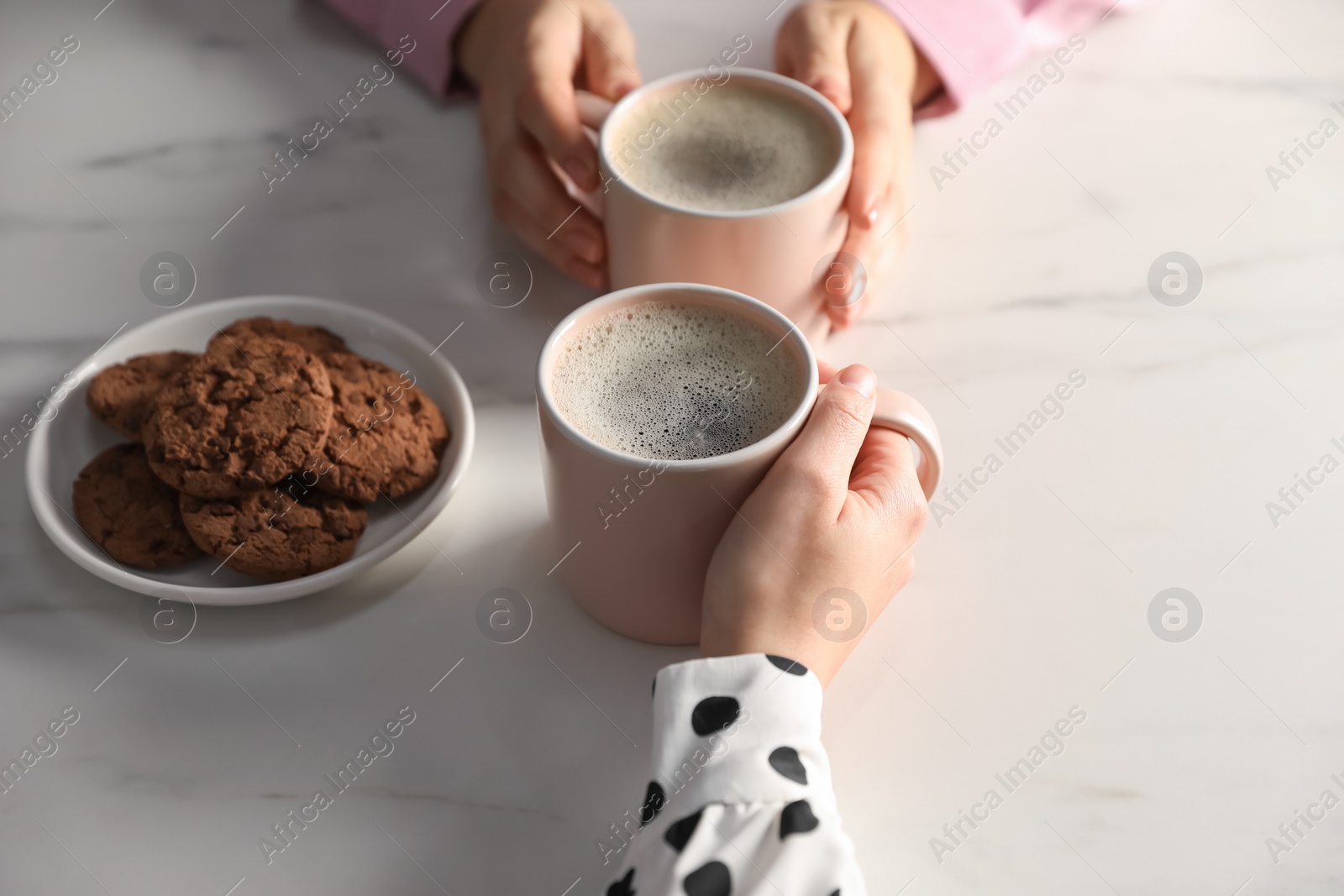 Photo of Women with cups of hot coffee and cookies at white marble table, closeup