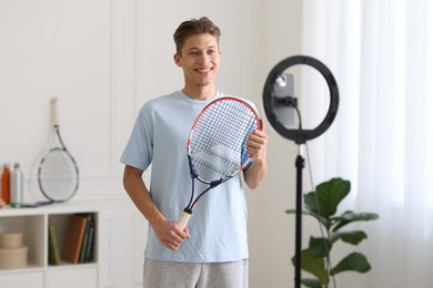 Smiling sports blogger holding tennis racket while streaming online fitness lesson at home