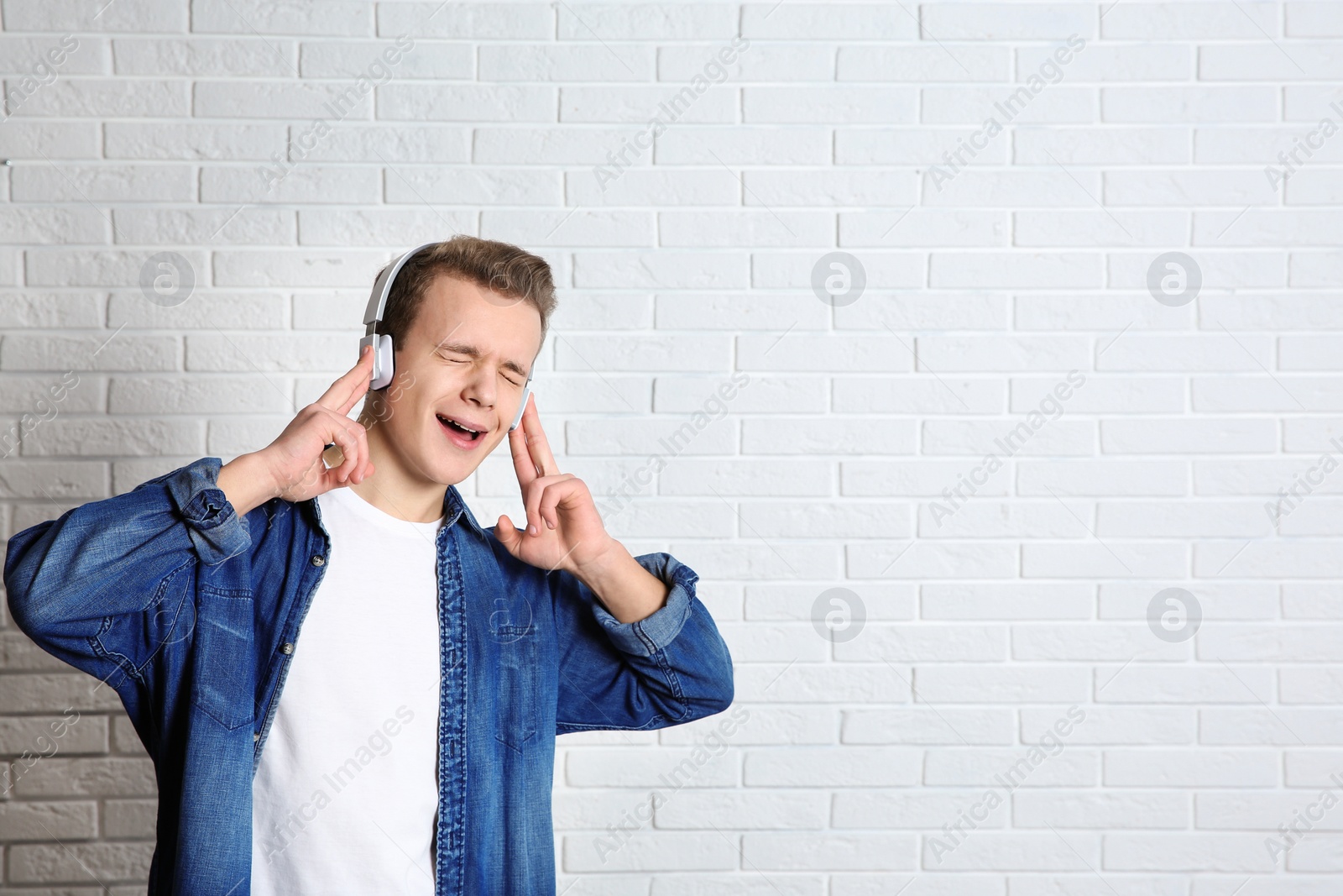 Photo of Teen boy listening to music with headphones near brick wall, space for text