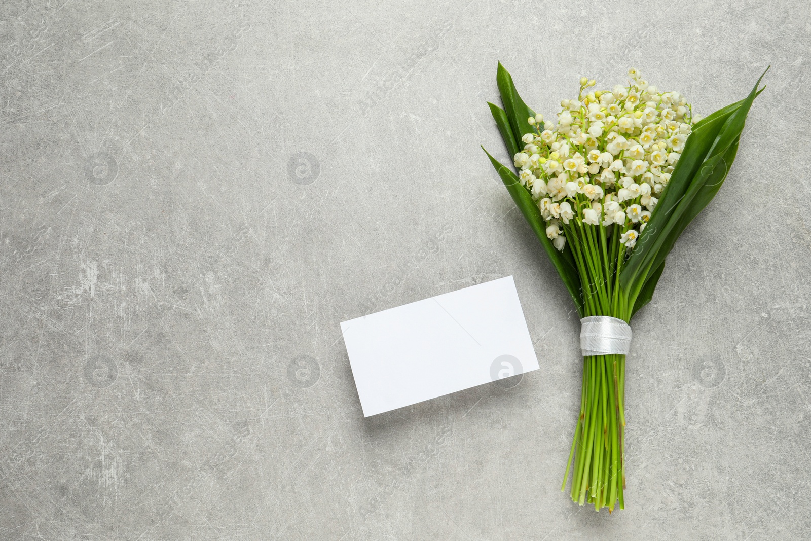 Photo of Beautiful lily of the valley bouquet and blank card on grey table, flat lay. Space for text