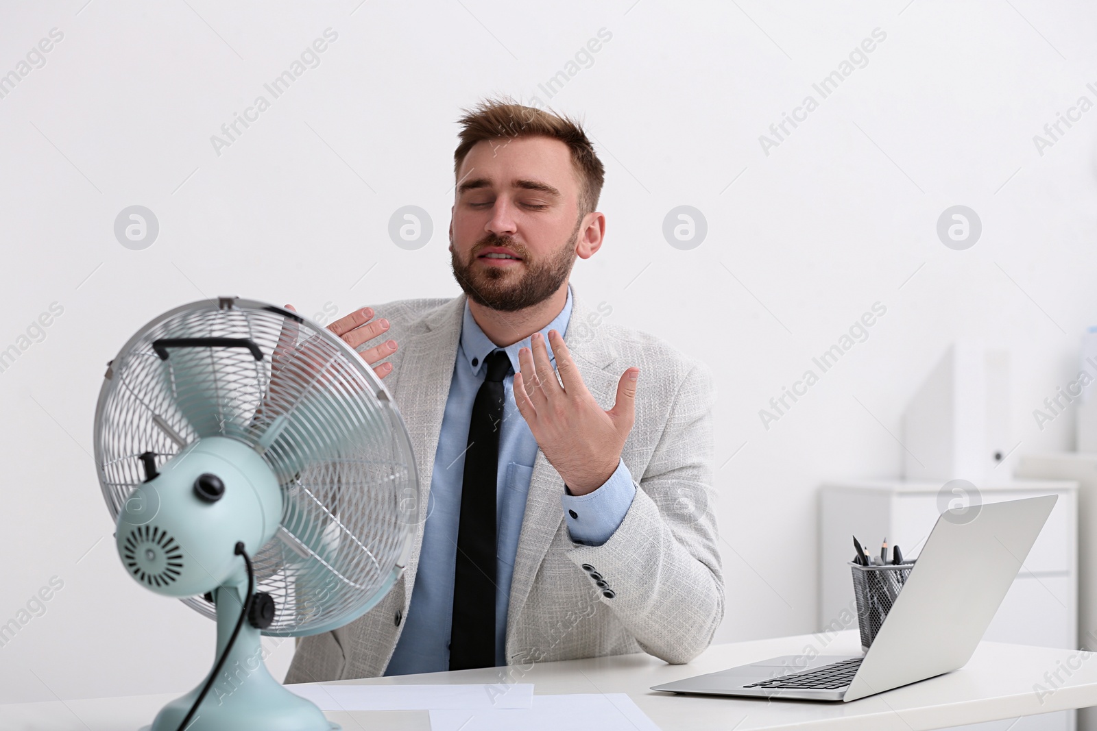 Photo of Man enjoying air flow from fan at workplace