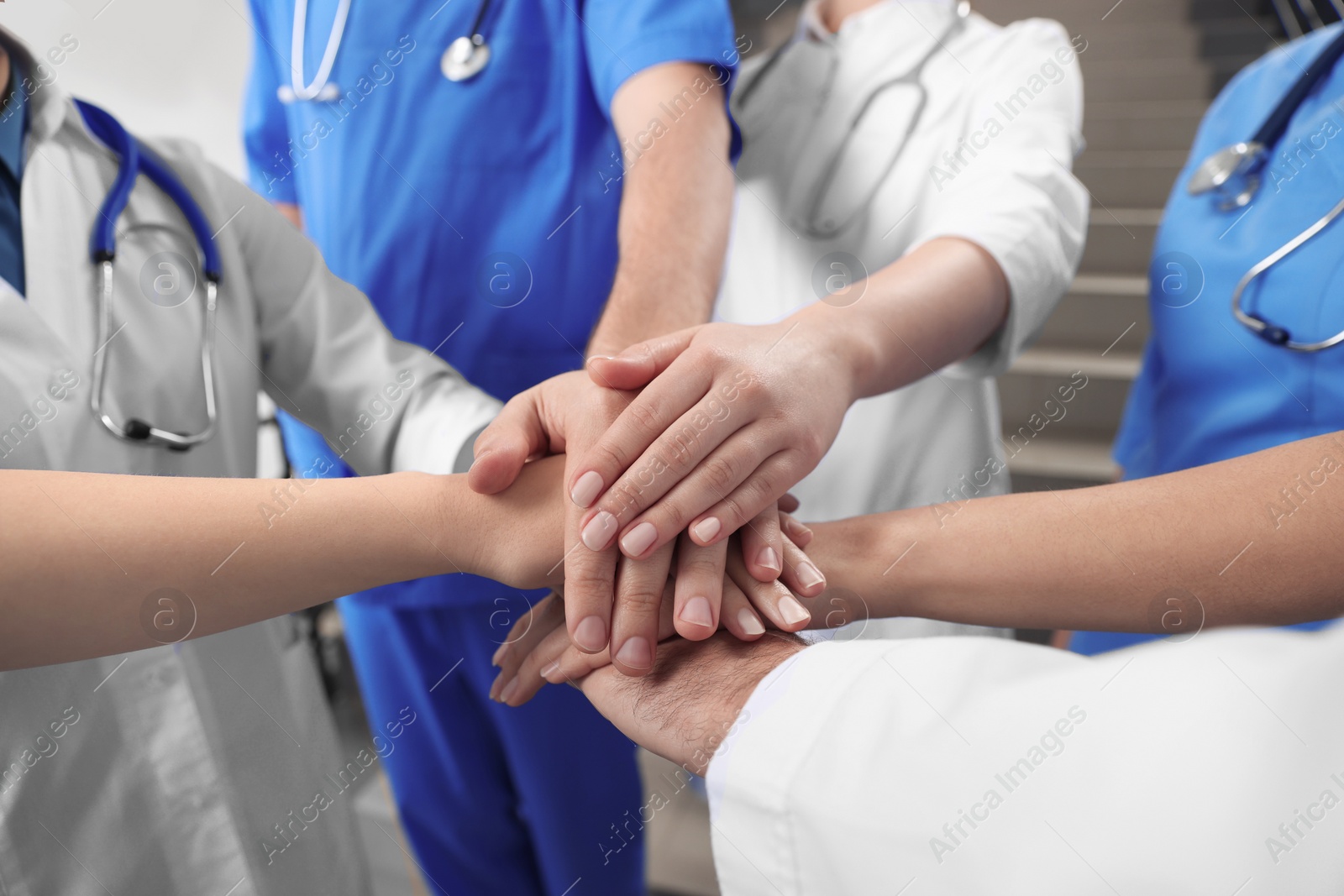 Photo of Team of medical doctors putting hands together indoors, closeup