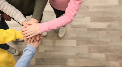 Photo of Group of people holding their hands together indoors, top view. Space for text