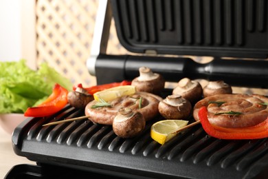 Photo of Electric grill with homemade sausages, bell pepper and mushrooms on table, closeup