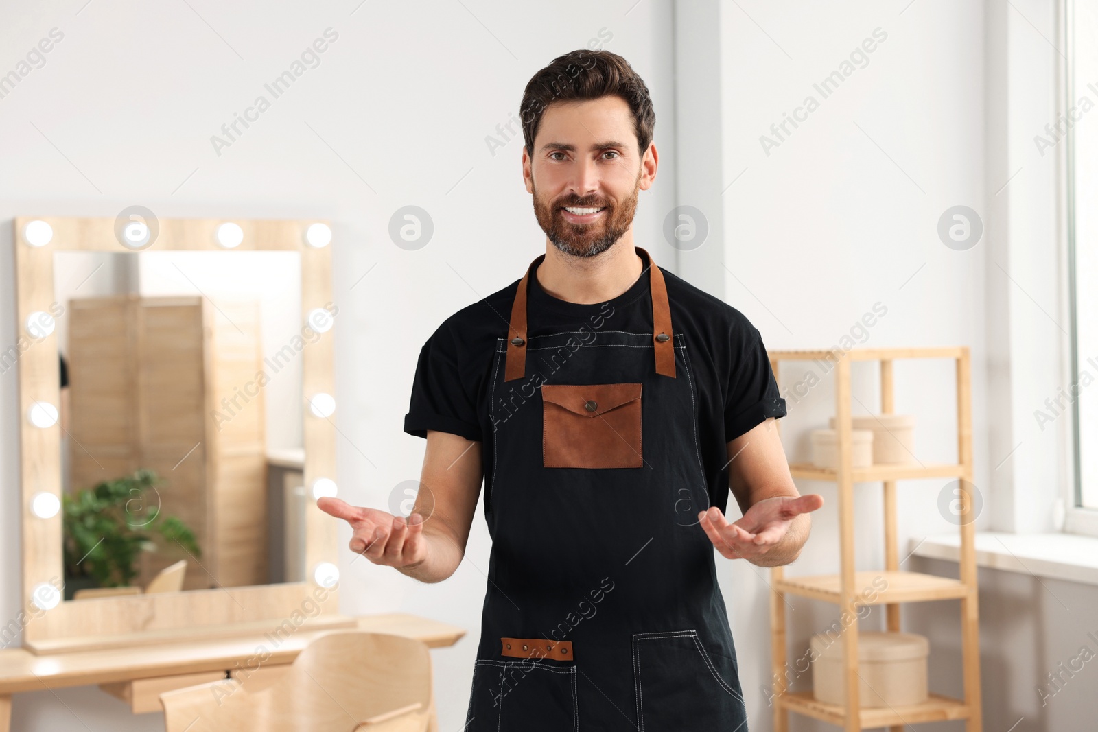 Photo of Smiling hairdresser wearing apron near vanity mirror in salon