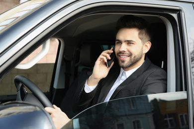Photo of Handsome young man talking on smartphone while driving his car