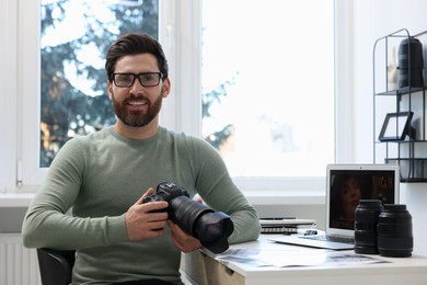 Photo of Professional photographer in glasses holding digital camera at table in office