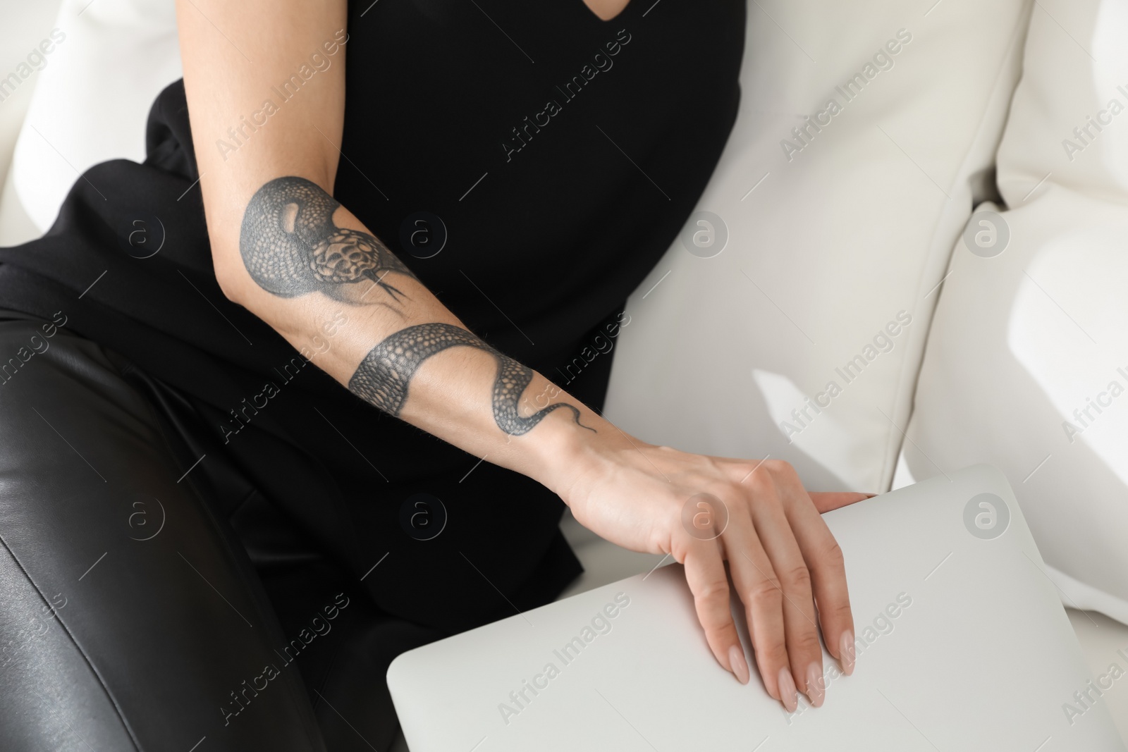 Photo of Beautiful woman with tattoos on arm using laptop indoors, closeup