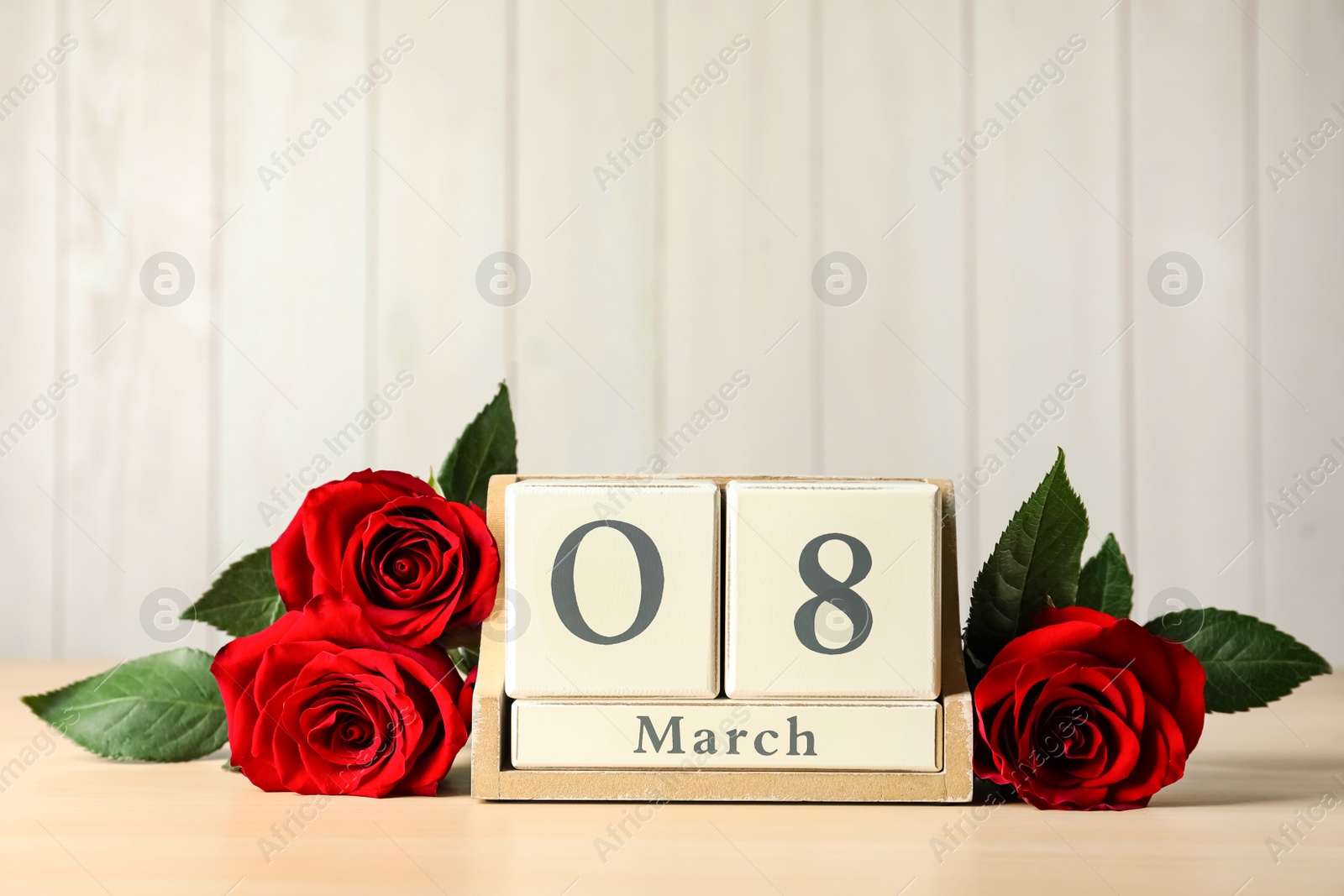 Photo of Wooden block calendar with date 8th of March and roses on table against light background, space for text. International Women's Day