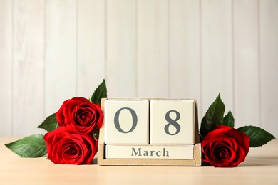 Wooden block calendar with date 8th of March and roses on table against light background, space for text. International Women's Day
