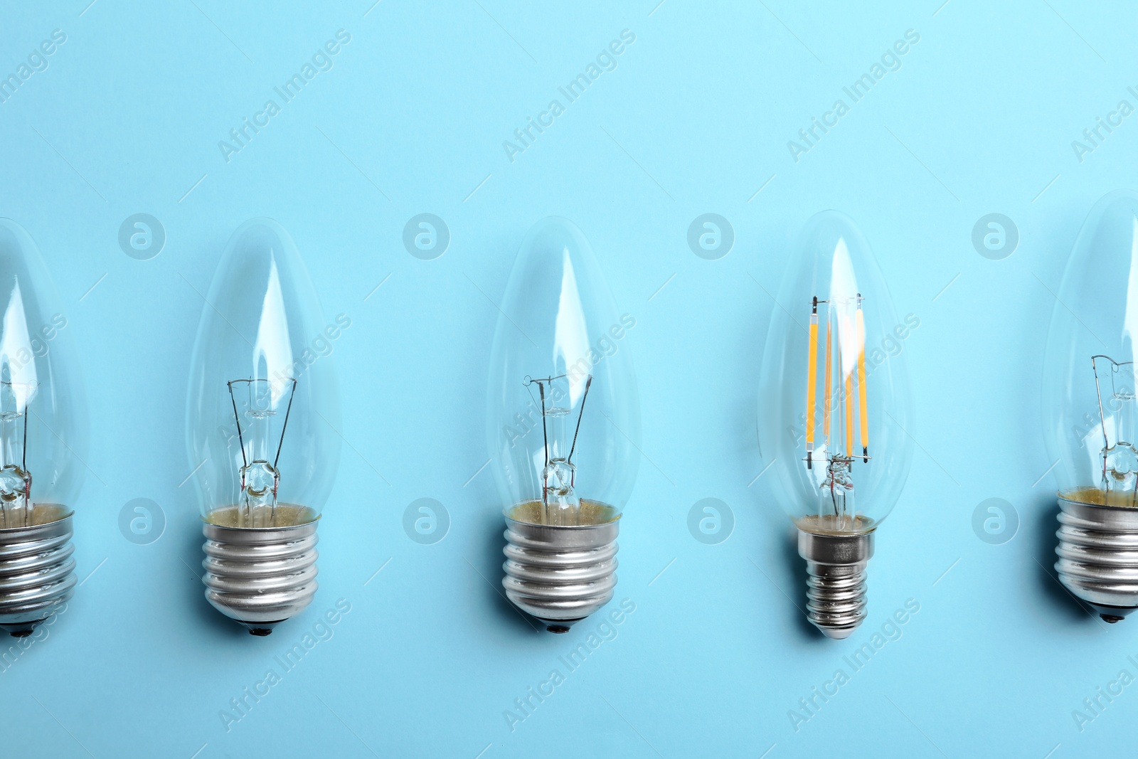 Photo of Vintage and modern lamp bulbs on light blue background, flat lay