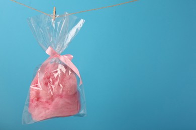Photo of Packaged sweet pink cotton candy hanging on clothesline against light blue background, space for text