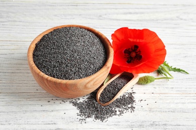 Photo of Wooden bowl of poppy seeds, scoop and flower on white table