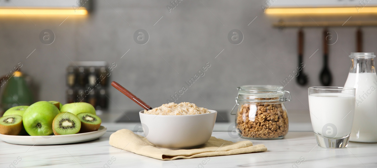 Photo of Breakfast time. Tasty oatmeal in bowl, fruits, granola and milk on white marble table. Banner design