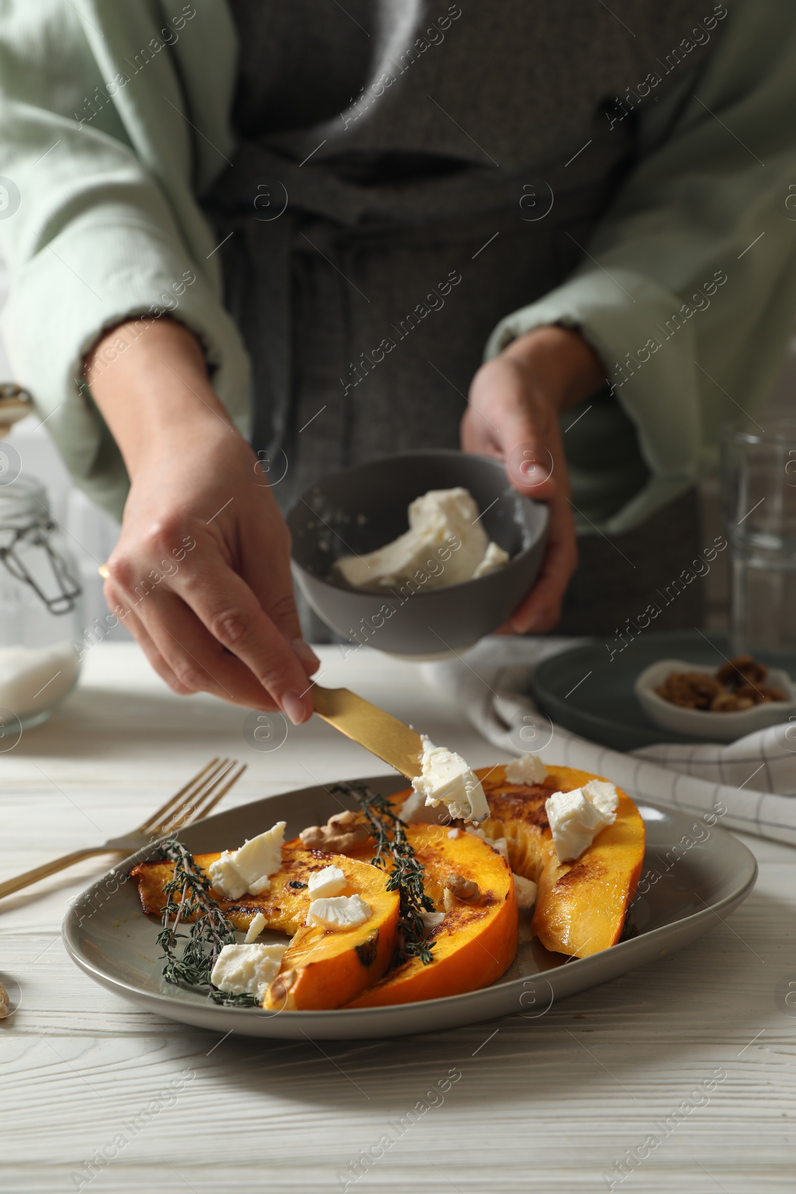 Photo of Woman putting cheese on baked pumpkin slices at table, closeup