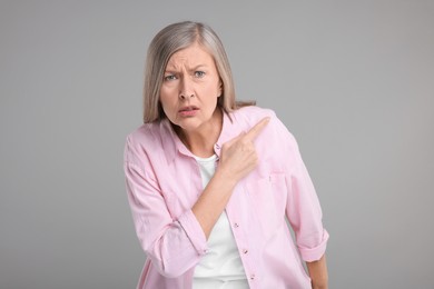 Surprised senior woman pointing at something on grey background