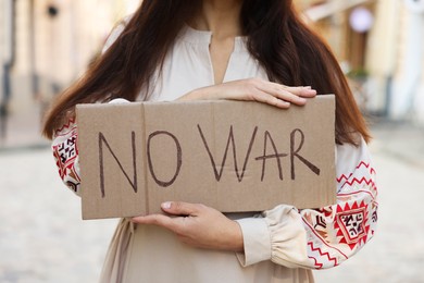 Photo of Woman in embroidered dress holding poster No War on city street, closeup