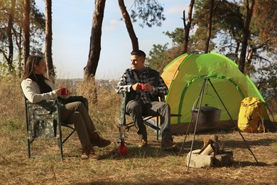 Photo of Couple resting in camping chairs and enjoying hot drink outdoors