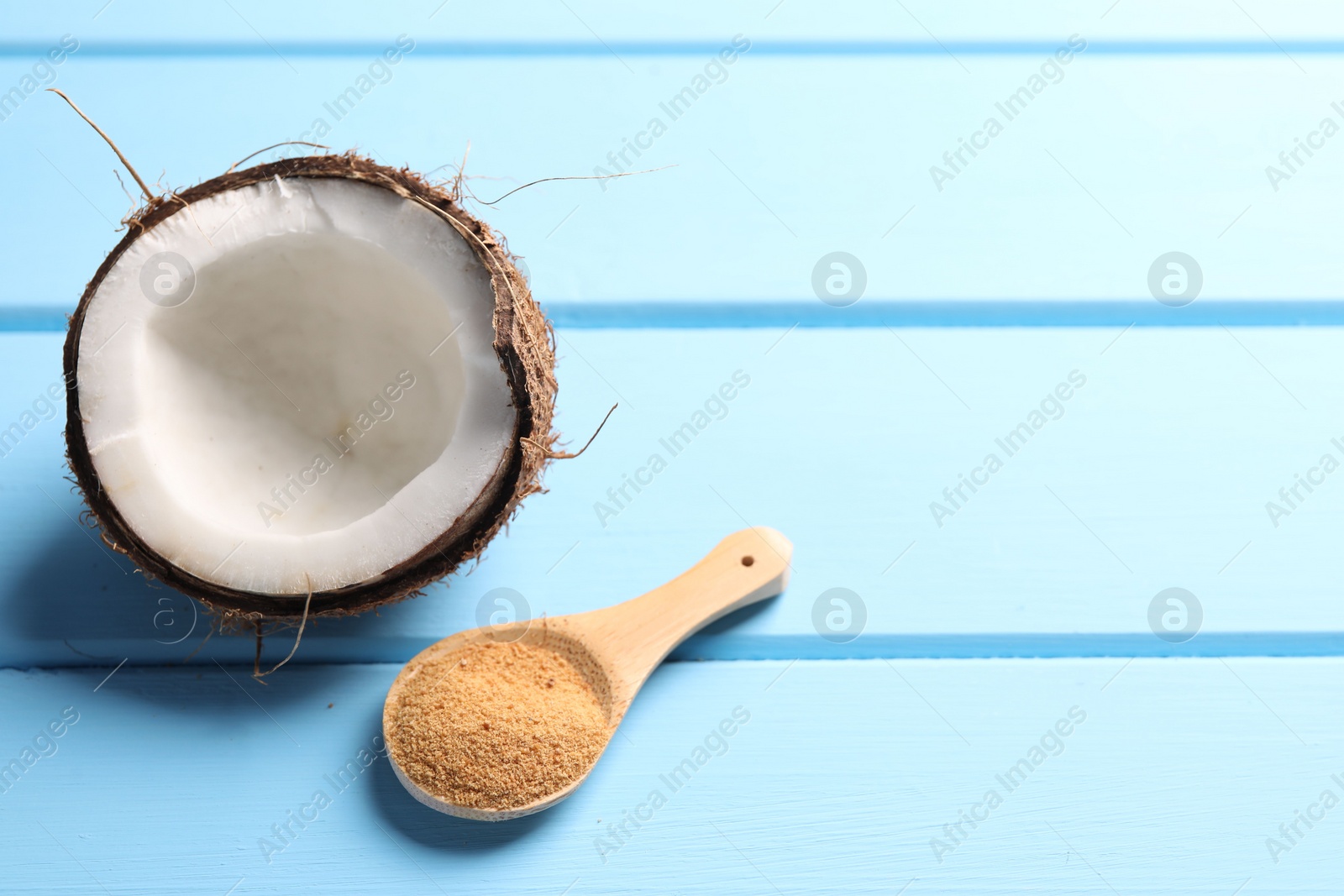 Photo of Spoon with coconut sugar and half of fruit on light blue wooden table, closeup. Space for text