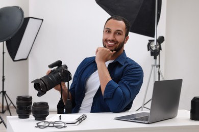 Young professional photographer with camera at table in modern photo studio