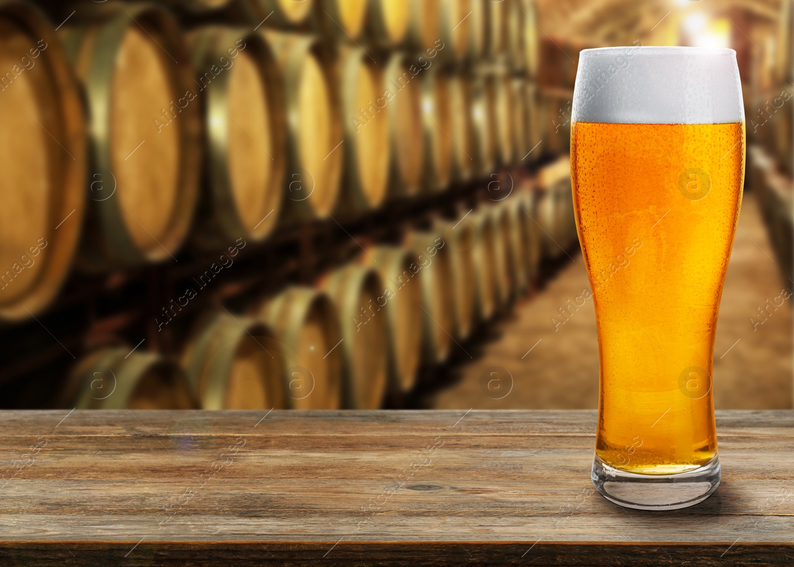 Image of Glass of tasty beer on wooden table in cellar with large barrels, space for text