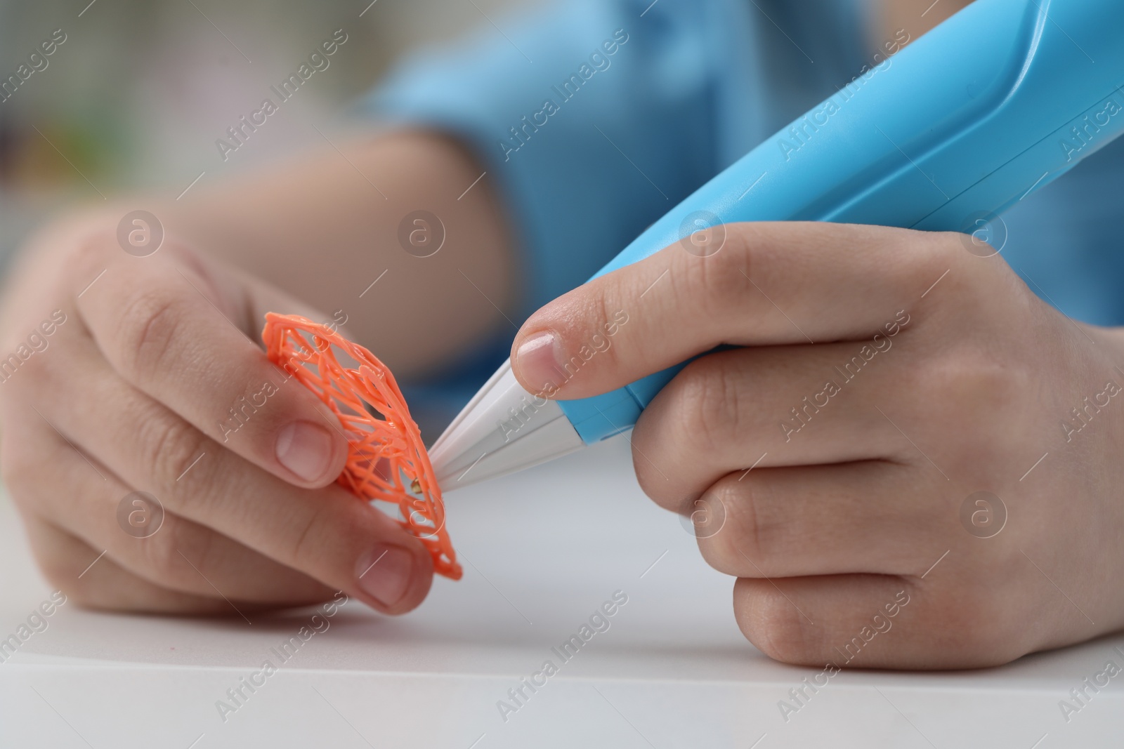 Photo of Girl drawing with stylish 3D pen at white table indoors, closeup