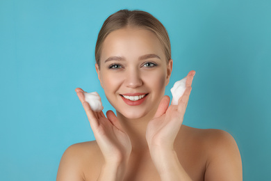 Young woman washing face with cleansing foam on light blue background. Cosmetic product