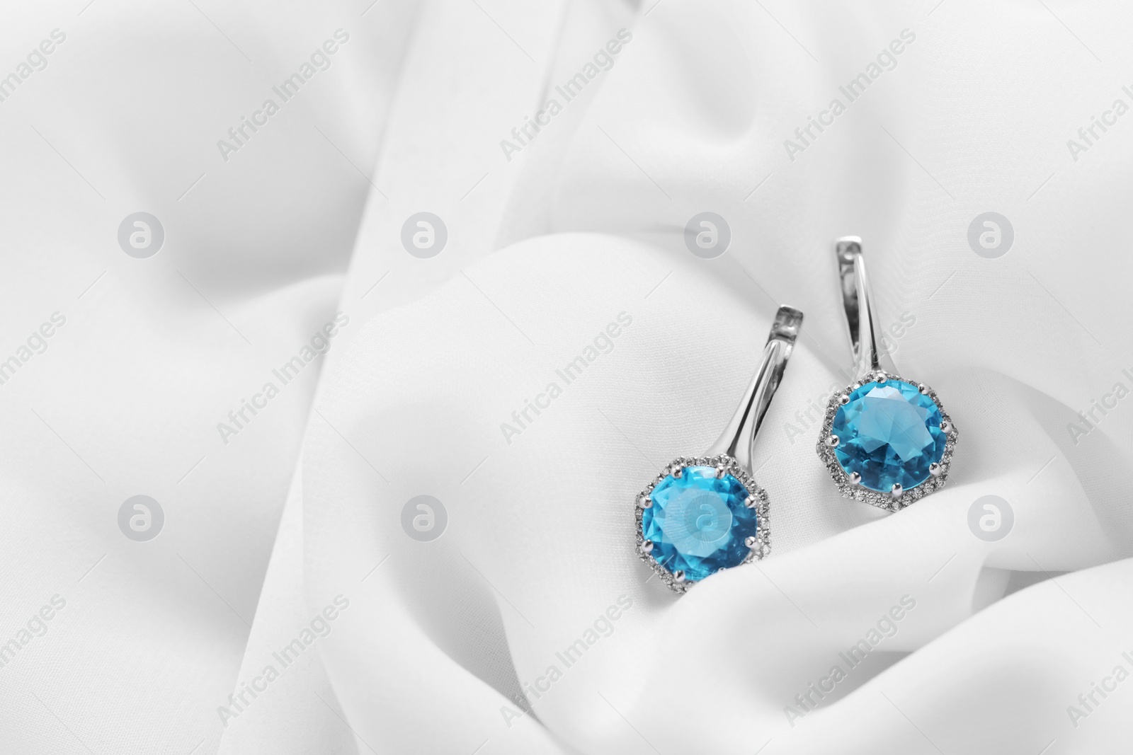 Photo of Beautiful earrings with light blue gemstones on white fabric, space for text. Luxury jewelry