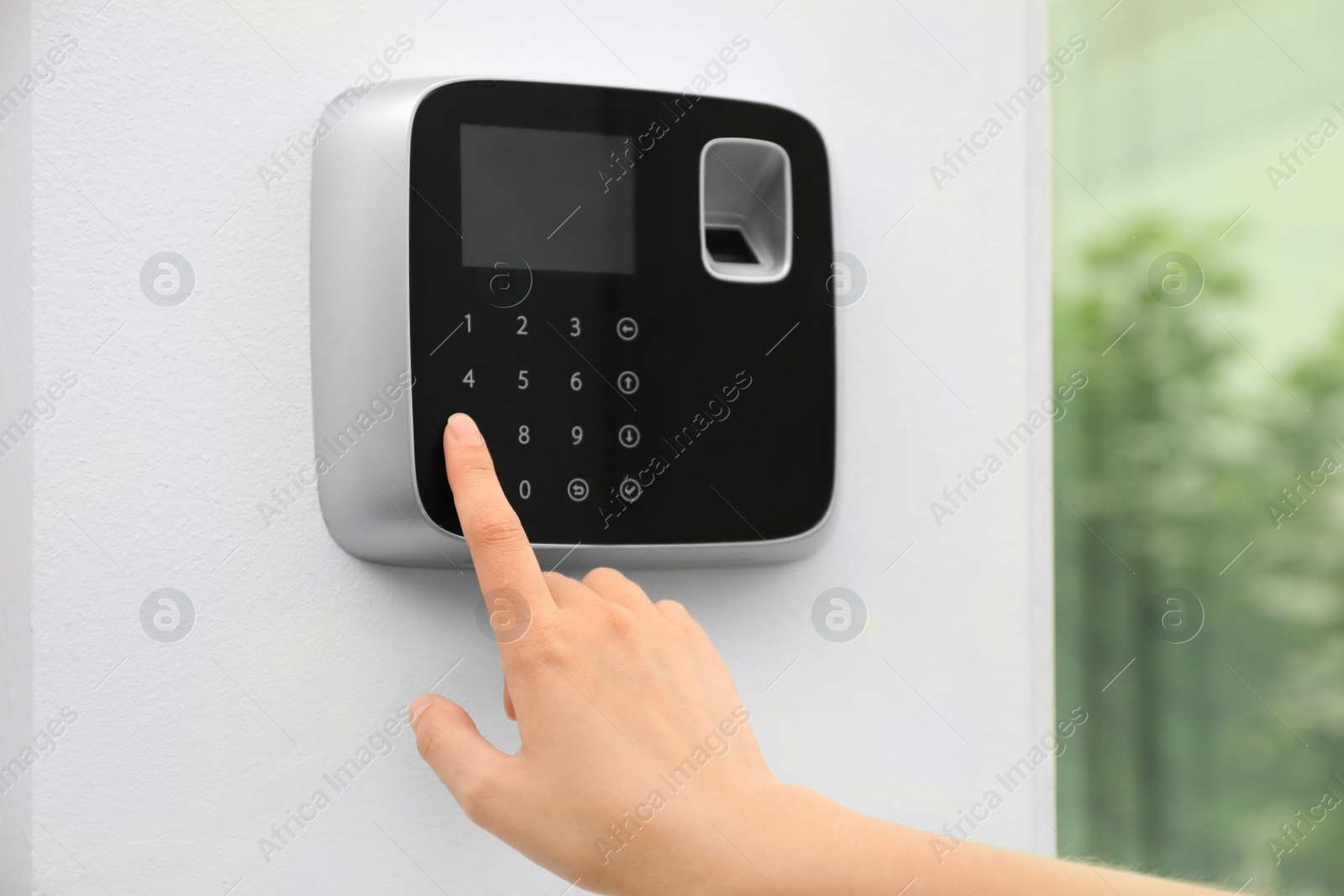 Photo of Young woman entering code on alarm system keypad indoors