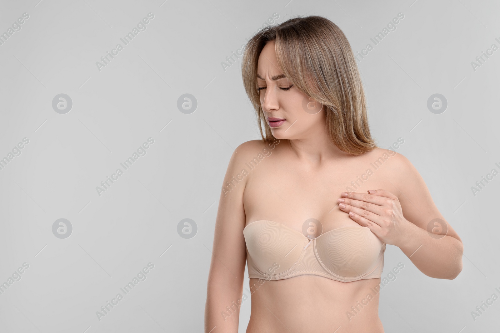 Photo of Mammology. Young woman doing breast self-examination on light grey background, space for text