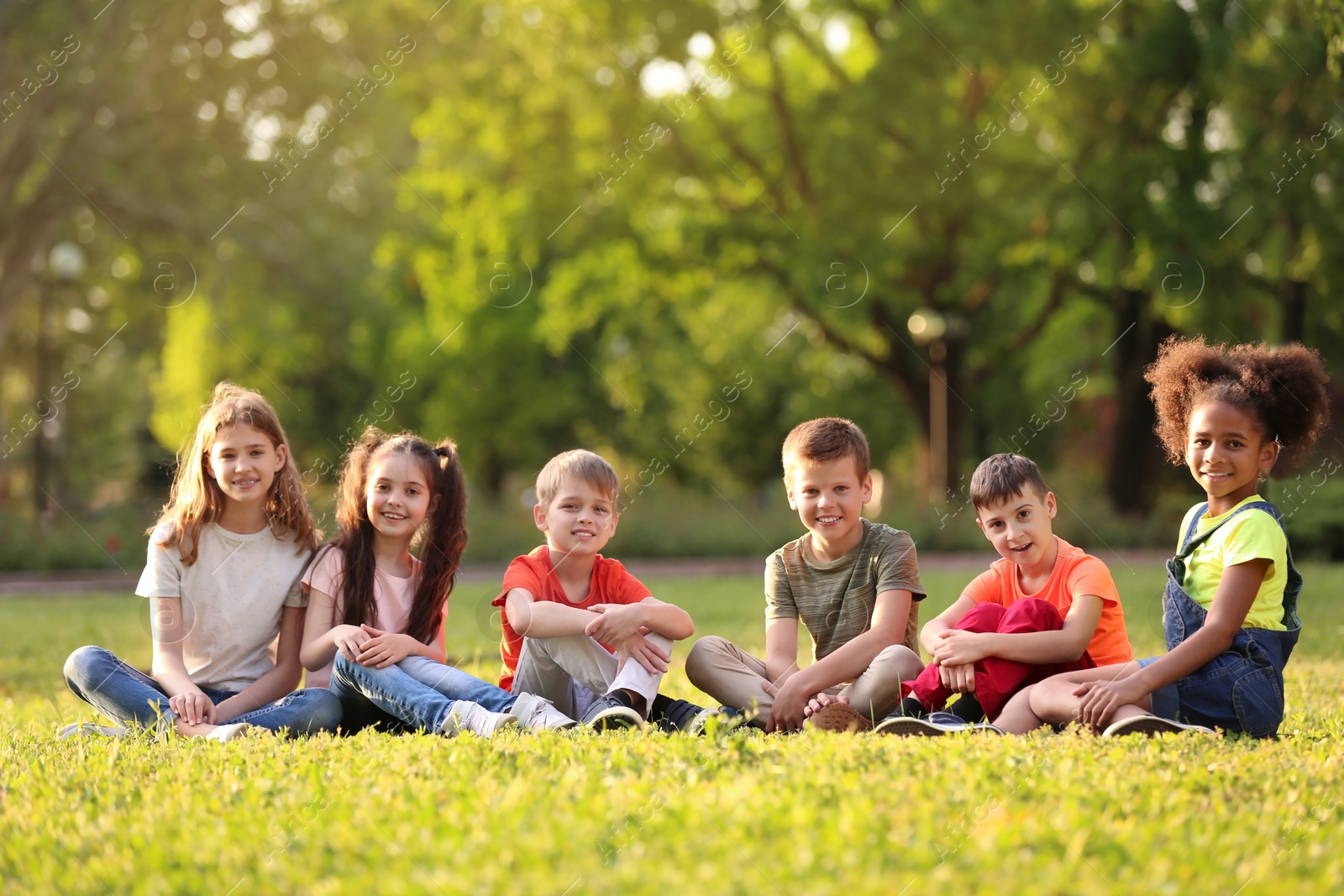 Photo of Cute little children sitting on grass outdoors on sunny day