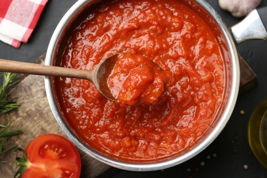 Photo of Homemade tomato sauce and spoon in pot on dark table, flat lay