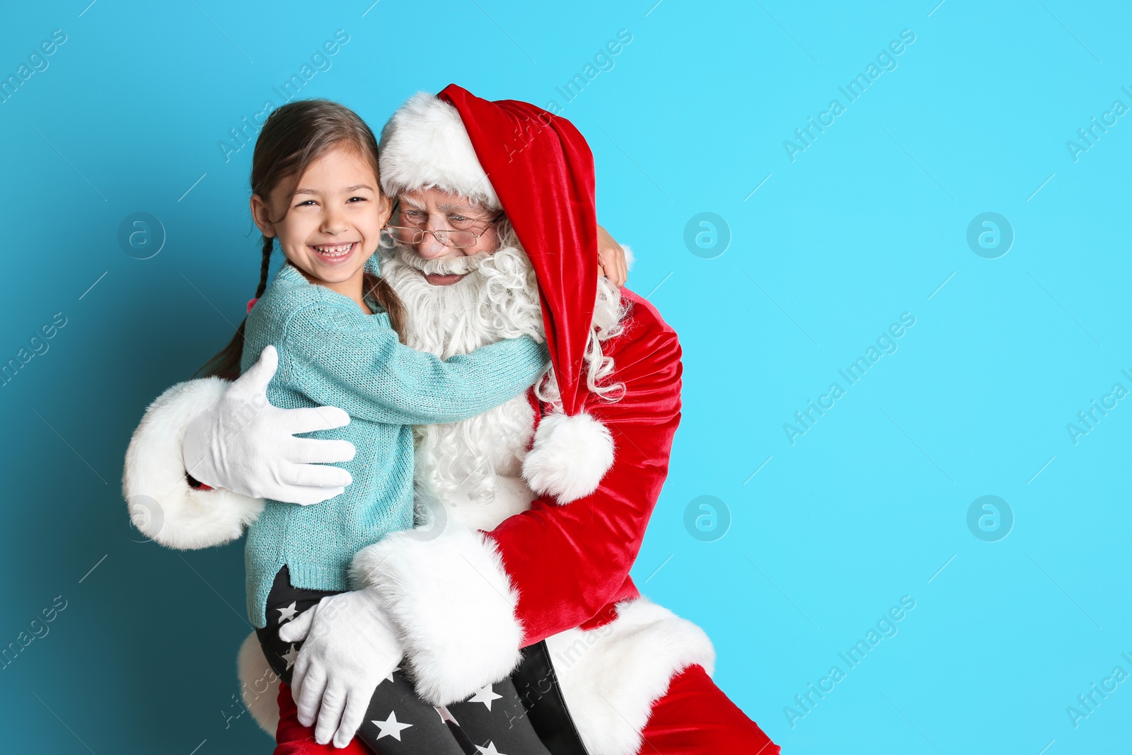 Photo of Little girl hugging authentic Santa Claus on color background